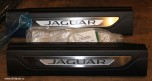 Комплект накладок порогов передних дверей с подсветкой Jaguar XF 2016 - 2024, стандартная база. Цвет пластиковой части: Jet (черный). Запчасть оригинальная новая Land Rover, в оригинальной коробке.